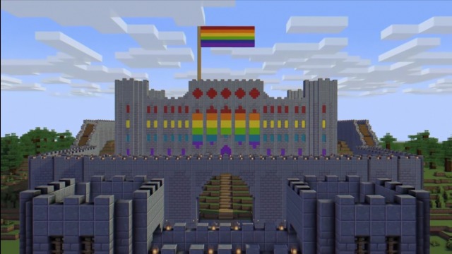 This is a screenshot from a Minecraft stream. It is unknown whose stream it originates from. The screenshot shows a smaller stone arch with two towers that welcome a visitor entering the castle. Behind that is the stone castle itself with large stone walls that surround it. An arch shows wooden stairs leading up to the main castle. The castle is formidable and tall with many windows. Each of the windows have colored concrete behind them in a rainbow pattern. Looking at all the windows at once reveals the lgbt+ or gay pride flag. Above the castle, the same gay pride flag is hung. The landscape around the castle is barren, with most trees chopped down.